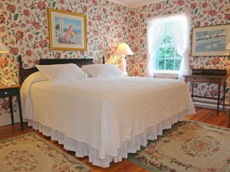 A cozy bedroom with floral wallpaper, a large bed with white bedding, two side tables with lamps, and framed artwork on the walls.