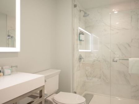A modern bathroom with a marble shower, toilet, and illuminated mirror above the vanity, creating an elegant, clean look.