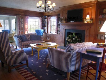 A cozy living room with striped furniture, a yellow coffee table, a fireplace, and a TV. Stars and stripes rug adds a patriotic touch.