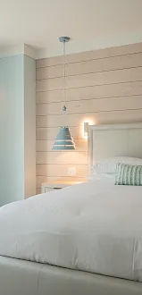 Modern bedroom with a neatly made bed, wood slat accent wall, pendant lights, and tall blue curtains by a window.